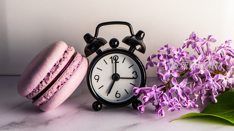 lilac flowers, macaroons and an alarm clock. selective focus. Macaroons and an alarm clock with a branch of flowers in lilac tones. Syrínga